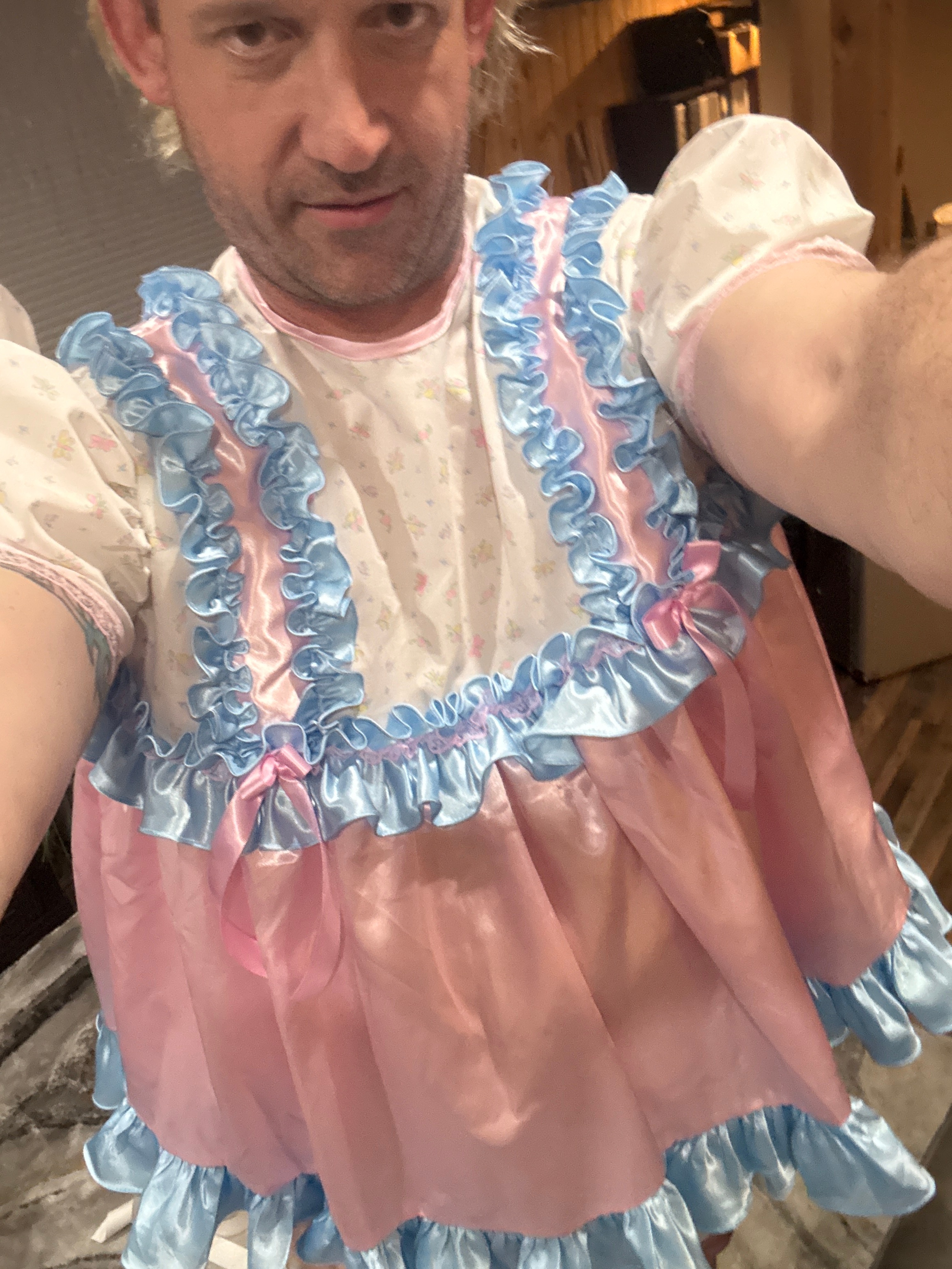 Close selfie of a man in a blue, pink, and white frilly outfit holding the camera indoors.