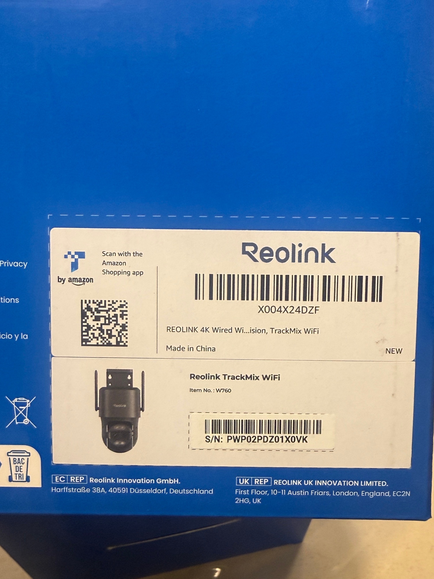 Blue Reolink camera package with white labels, barcodes, a QR code, and a small camera illustration on a tabletop.