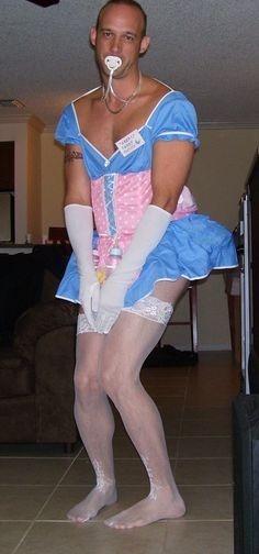 A person poses indoors in a blue dress with a pink lace-up bodice, white gloves, stockings, and a pacifier.